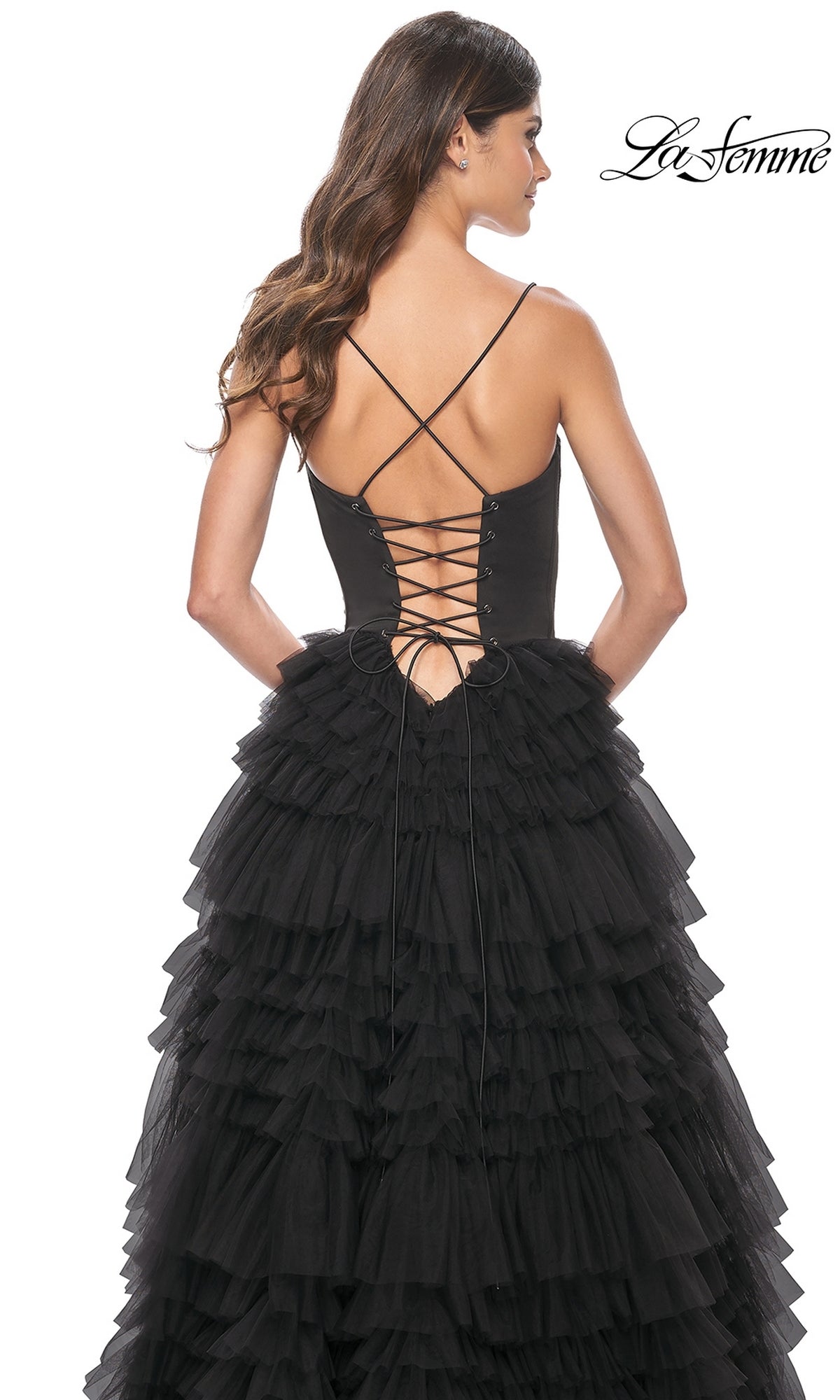 A woman is seen from the back wearing the La Femme 32071 Lace-Up Ruffle Long Prom Ball Gown, featuring a black lace-up sweetheart corset bodice and a layered tulle skirt.